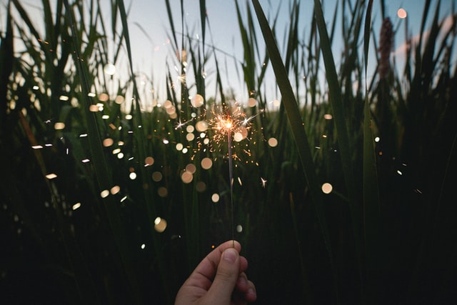 Woman's hand holding a lit sparkler in a field.