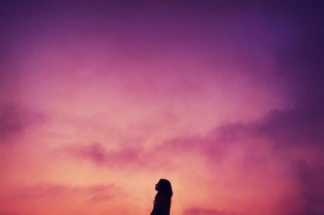 Silhouette of a woman in front of a purple sky, looking up.