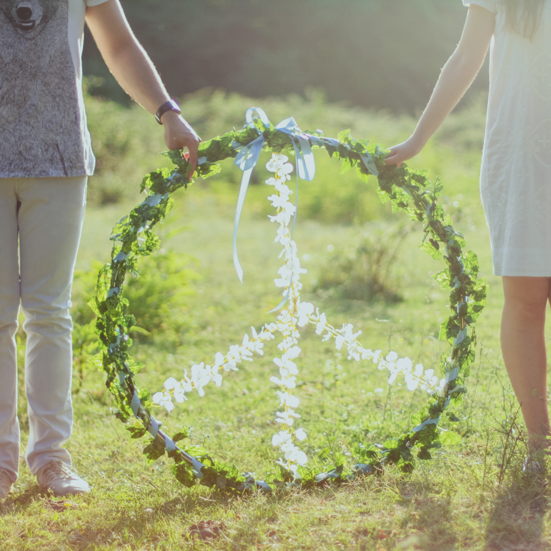 Peace Sign held by a couple- peace sign is hand made and wrapped in vines and flowers and the photo is taken outside during the day!